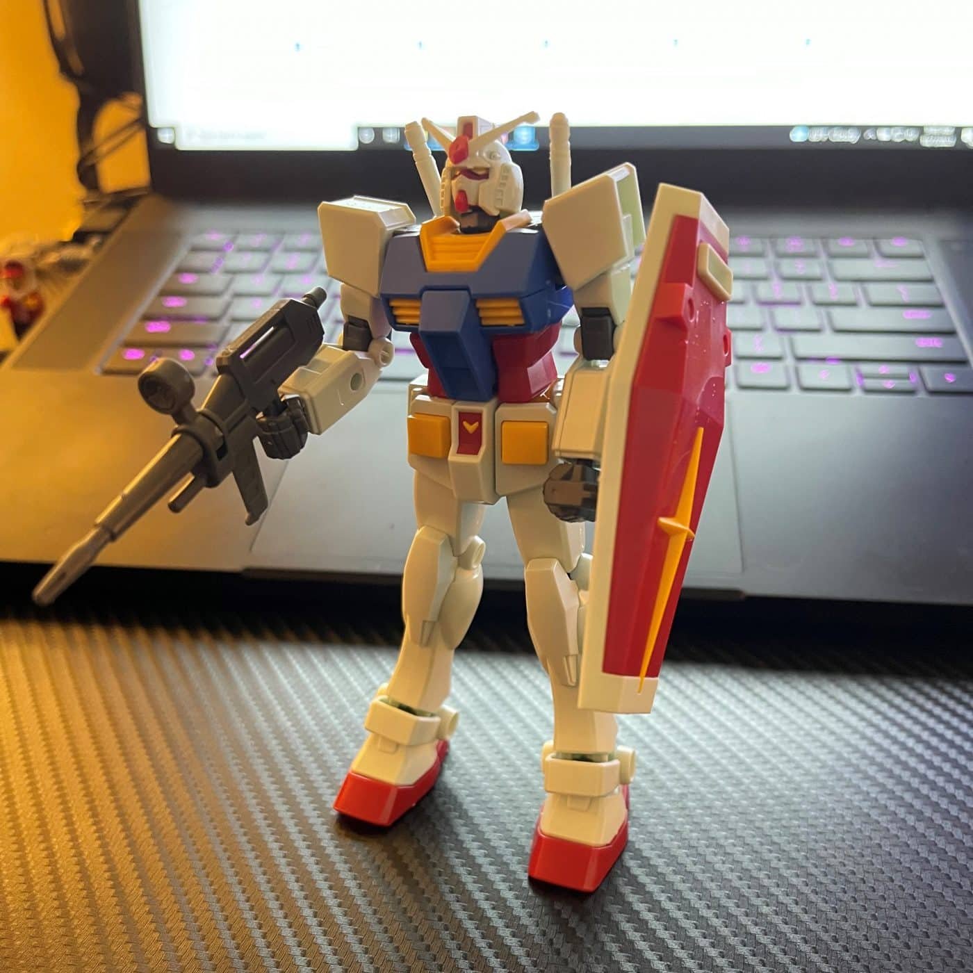 An entry grade gundam stands on a desk in front of a laptop